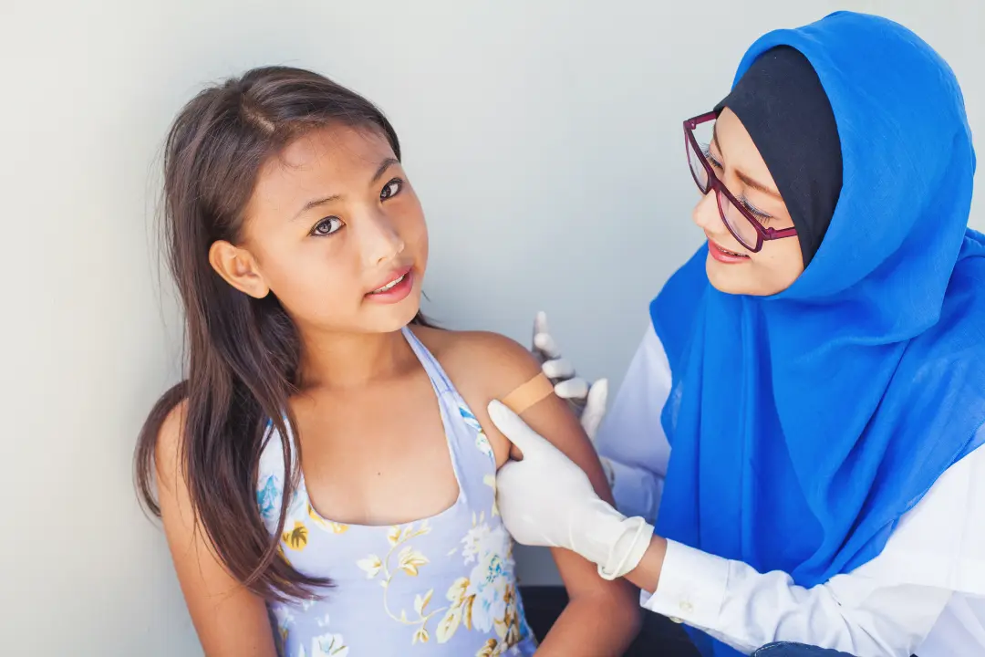 Asian muslim doctor sticking patch on hand of little asian girl